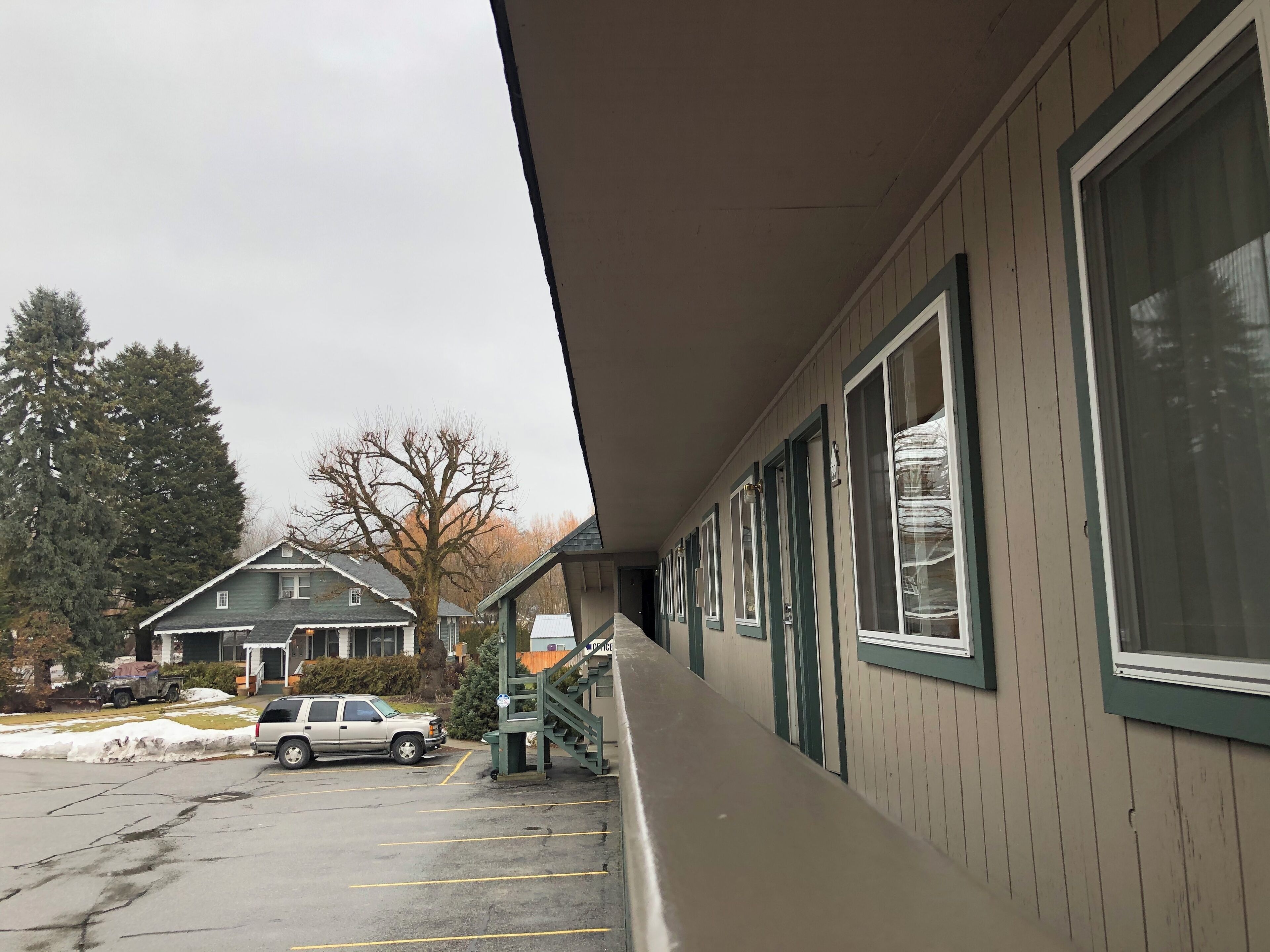 A motel with a covered walkway, a parking lot, and a neighboring house.