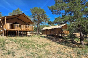 A wooden cabin with a balcony, surrounded by trees. - Eco Camping | Tente Lodge tout confort | Piscine (Saint-Laurent-du-Verdon)