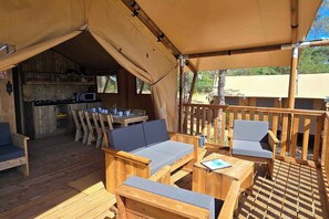 A wooden deck with a sofa, chairs, and a table. - Eco Camping | Tente Lodge tout confort | Piscine (Saint-Laurent-du-Verdon)