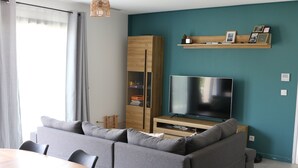 Uma sala de estar moderna com um sofá cinzento, um armário de madeira, uma televisão e uma mesa de jantar.