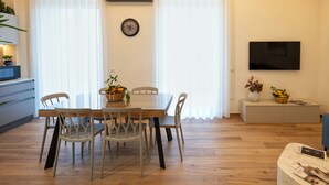 A modern living room with a dining area, featuring a wooden floor, a TV mounted on the wall, and a clock on the wall. - Central Pompeii Apt Near the Ruins, Free Parking (Pompei)