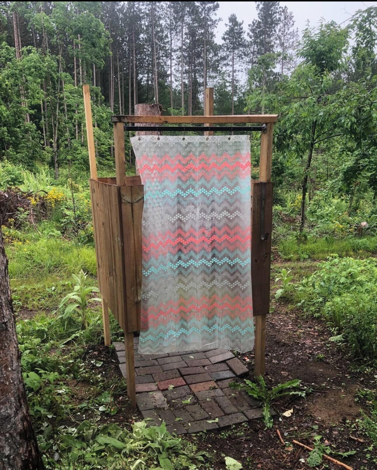 A wooden structure with a patterned fabric hanging from it, set in a forested area with a brick pathway.