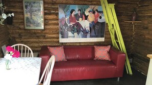 A cozy room with a red leather sofa, a wooden dining table with a white floral tablecloth, and a painting on the wall.