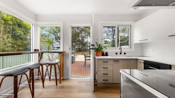 Una cucina moderna con mobili bianchi, una lavastoviglie in acciaio inossidabile e un terrazzo in legno con posti a sedere all'aperto.