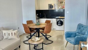 A modern living room with a dining area, a blue armchair, a sofa, and a kitchen in the background. - Beautiful, comfortable apartment just 10 minutes from the sea by car (VC)