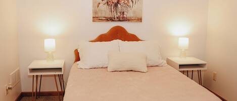 Un dormitorio con una cama grande, dos mesitas de noche con lámparas, un cabecero y un cuadro con motivos florales en la pared.
