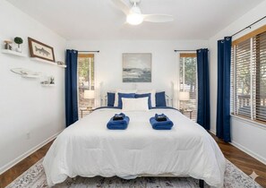 Une chambre à coucher avec un lit, un ventilateur de plafond, un tableau et une fenêtre avec des rideaux.