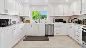 Een moderne keuken met witte kasten, roestvrijstalen apparatuur en een raam dat voor natuurlijk licht zorgt.