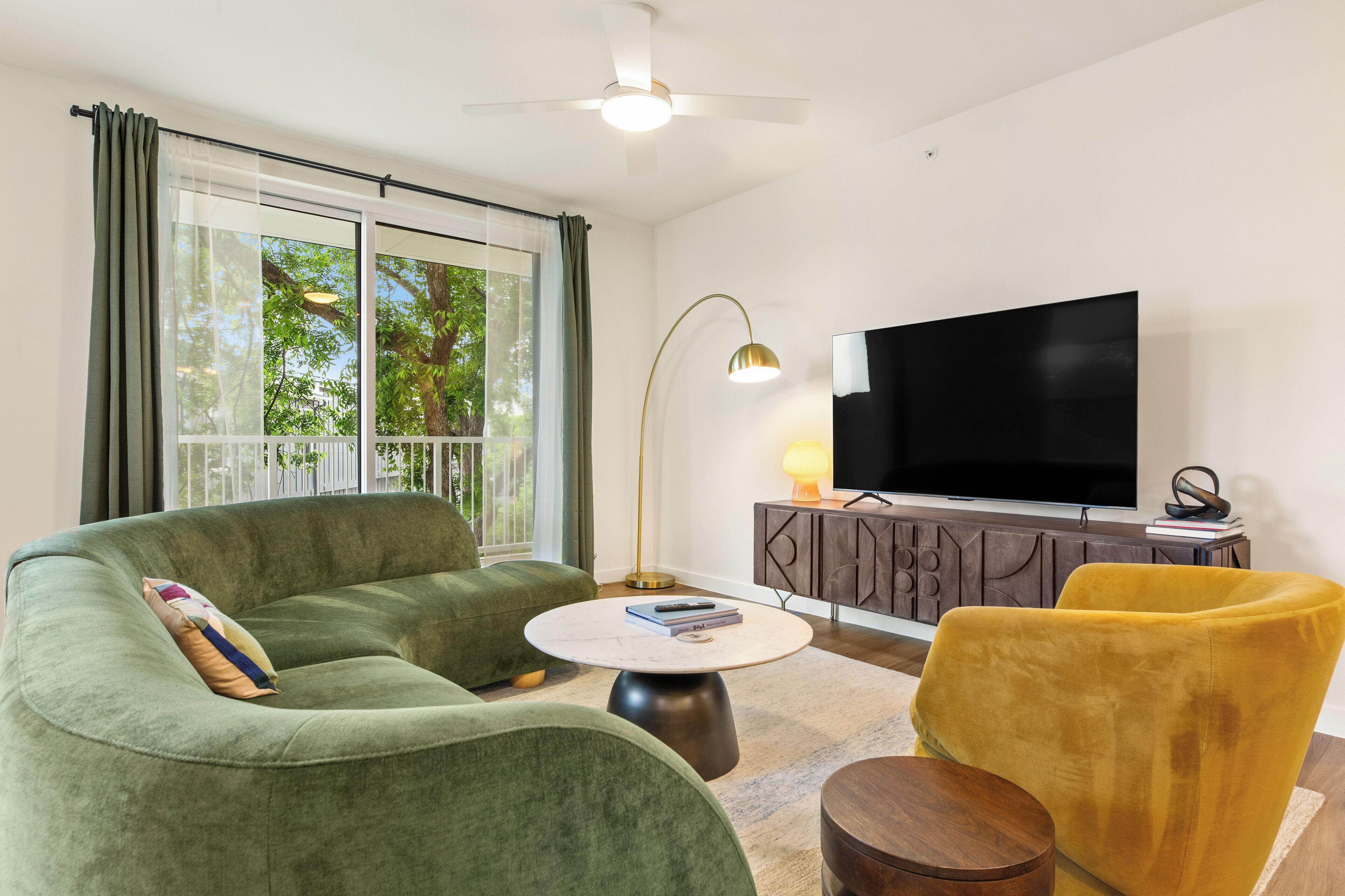 A living room with a sofa, a yellow chair, a round coffee table, a TV, and a cabinet.