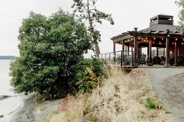 Une structure en bois située au bord du lac, dotée d’un espace extérieur aménagé et offrant une vue sur l’eau.