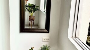 Ein kleiner, heller Holztisch mit dunklem Metallgestell, ein Spiegel mit dunklem Rahmen und ein Blumentopf.