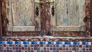 A rustic wooden door with green and white distressed paint, two green handles, and a decorative metal latch.