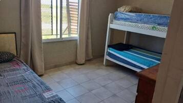 A small room with a bunk bed, a single bed, a window with curtains, and a tiled floor.
