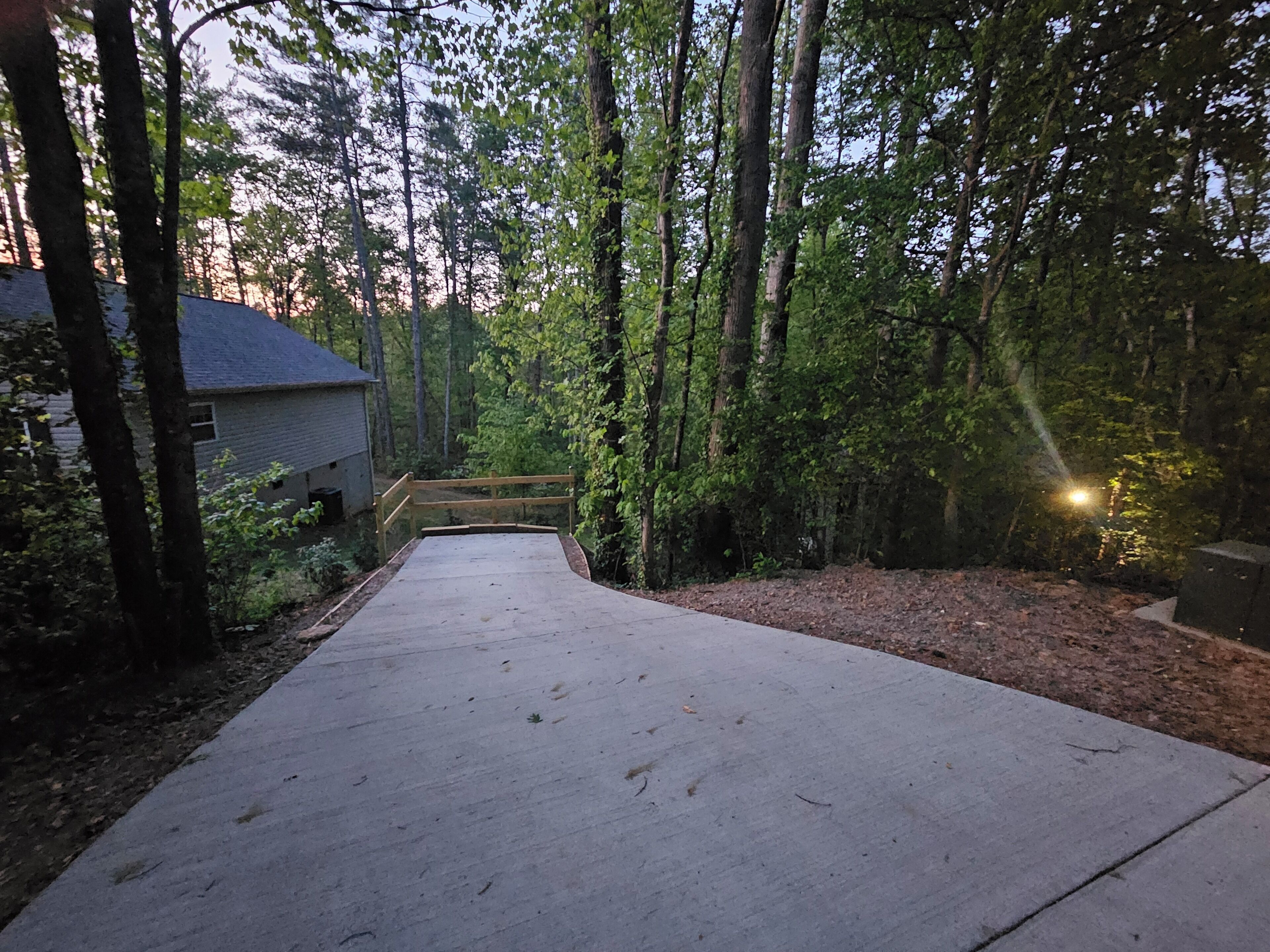 Um caminho de concreto leva a uma casa cercada por árvores.