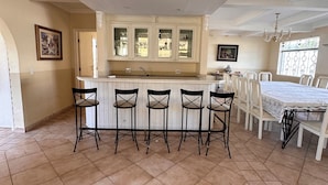 A kitchen with a central island, bar stools, and a dining area with a table and chairs. - House in Guarujá with Pool and Hot Tub • Near the Beach (Guarujá)
