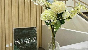 A reception desk with a vase of white flowers and a framed sign with the name 'Brenthill' and contact information. - Cherisia's Hideaway (Baguio)