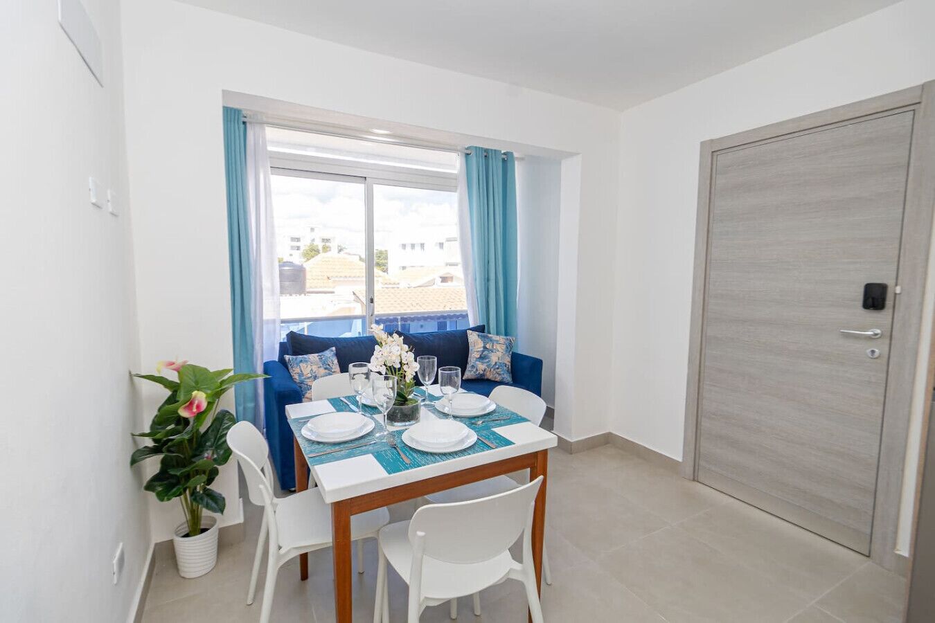 Un coin repas avec une table dressée pour quatre personnes, un canapé bleu et une plante en pot.