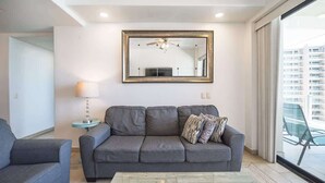 Uma sala de estar moderna com um sofá cinzento, uma mesa lateral com abajur e um espelho grande na parede.
