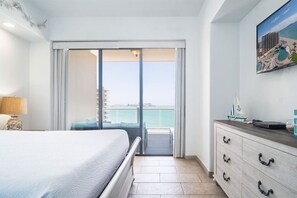 A hotel room with a bed, a dresser, a lamp, and a view of the sea through a sliding door.