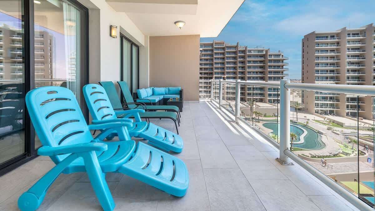 Een balkon met blauwe loungestoelen, een zwembad en hoge gebouwen op de achtergrond.