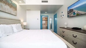 Ein Hotelzimmer mit Bett, Schminktisch, einem Gemälde und Blick auf einen Strand.