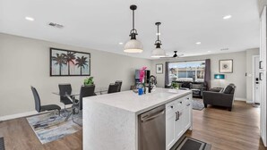 Una cocina moderna con una isla central, comedor con sillas y sala de estar con un sofá y televisor.