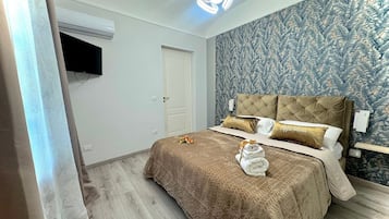 A bedroom with a bed, a wall-mounted TV, a door, and a patterned wallpaper.