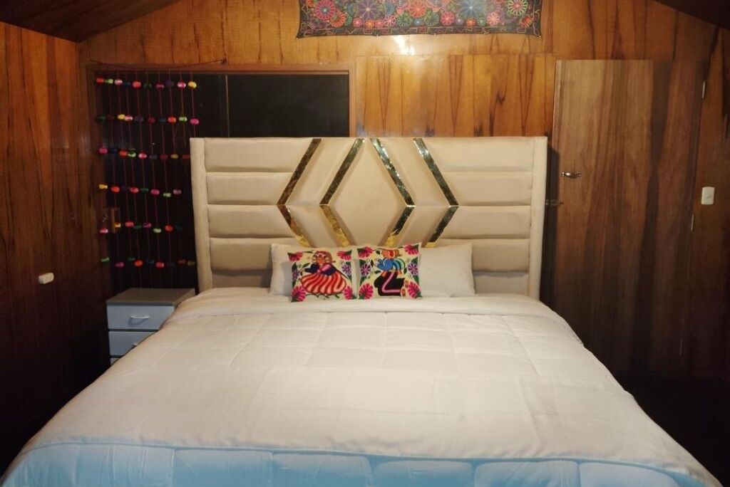 Ein Schlafzimmer mit einem hölzernen Kopfteil, einem Bett mit weißer Bettwäsche und farbenfrohen Kissen.