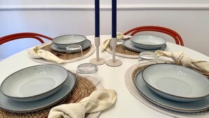 Ett runt matbord dukat med tallrikar, glas och servetter, med en vit vägg och röda stolar i bakgrunden.