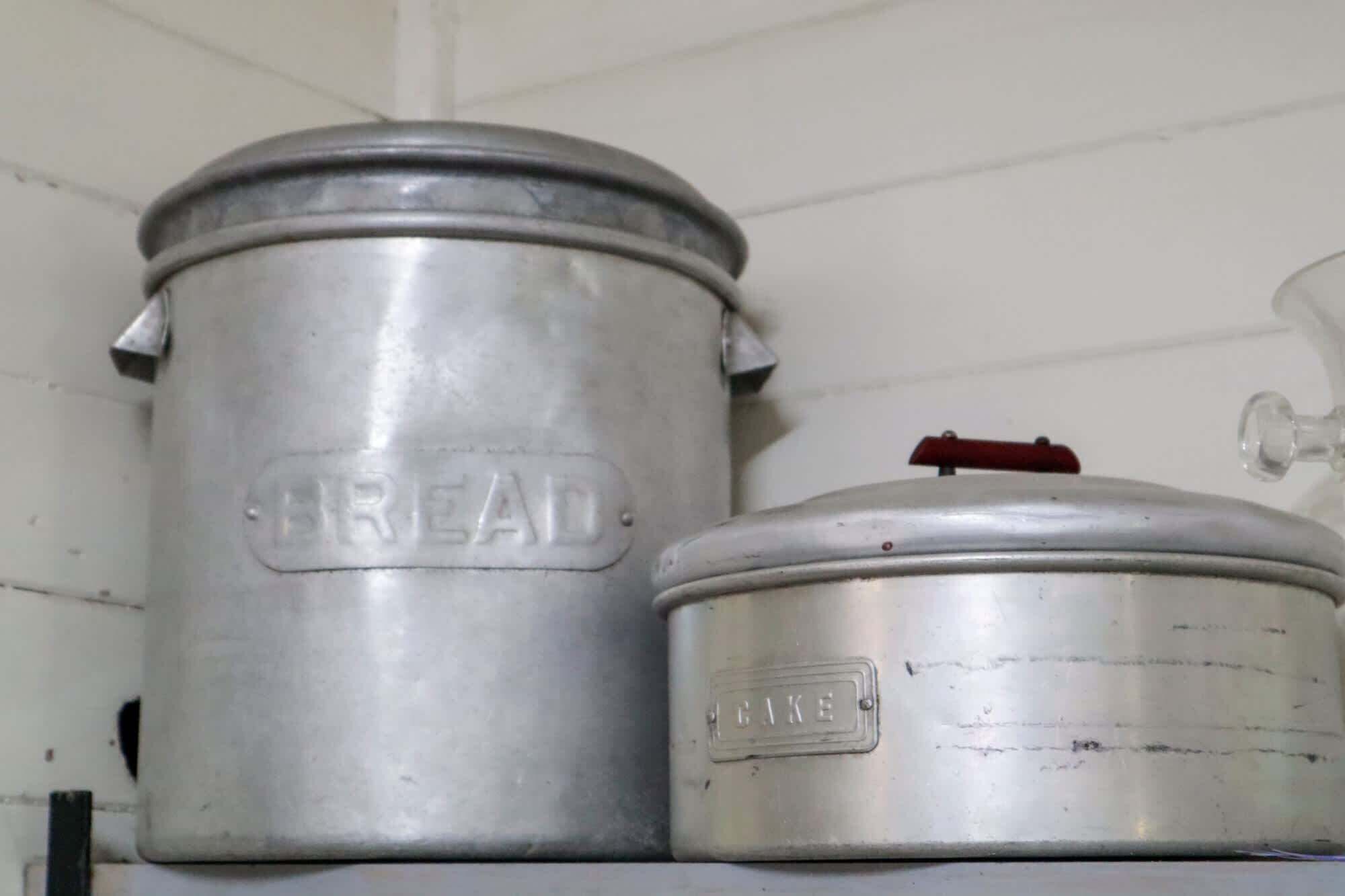 Two metal containers, one labeled "BREAD" and the other "CAKE," likely used for storage in a kitchen setting.