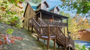 Eine Blockhütte mit einer Holzterrasse und einer Treppe zu einem Balkon im zweiten Stock.