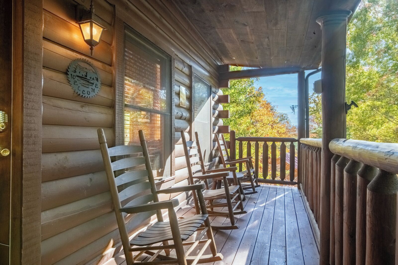 A wooden porch with rocking chairs, a welcome sign, and a view of trees.