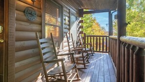 Eine Holzveranda mit Schaukelstühlen, einem Willkommensschild und Blick auf Bäume.