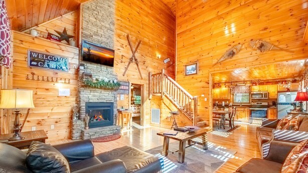 Ein gemütliches Blockhaus mit Kamin, Holzwänden, einer Treppe und einem Wohnbereich mit Sofas und einem Couchtisch.