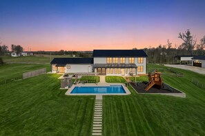 A two-story house with a swimming pool, a wooden play structure, and a well-maintained lawn.