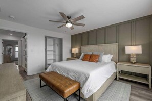 Une chambre moderne avec un grand lit, un ventilateur de plafond, des lampes de chevet et un banc.