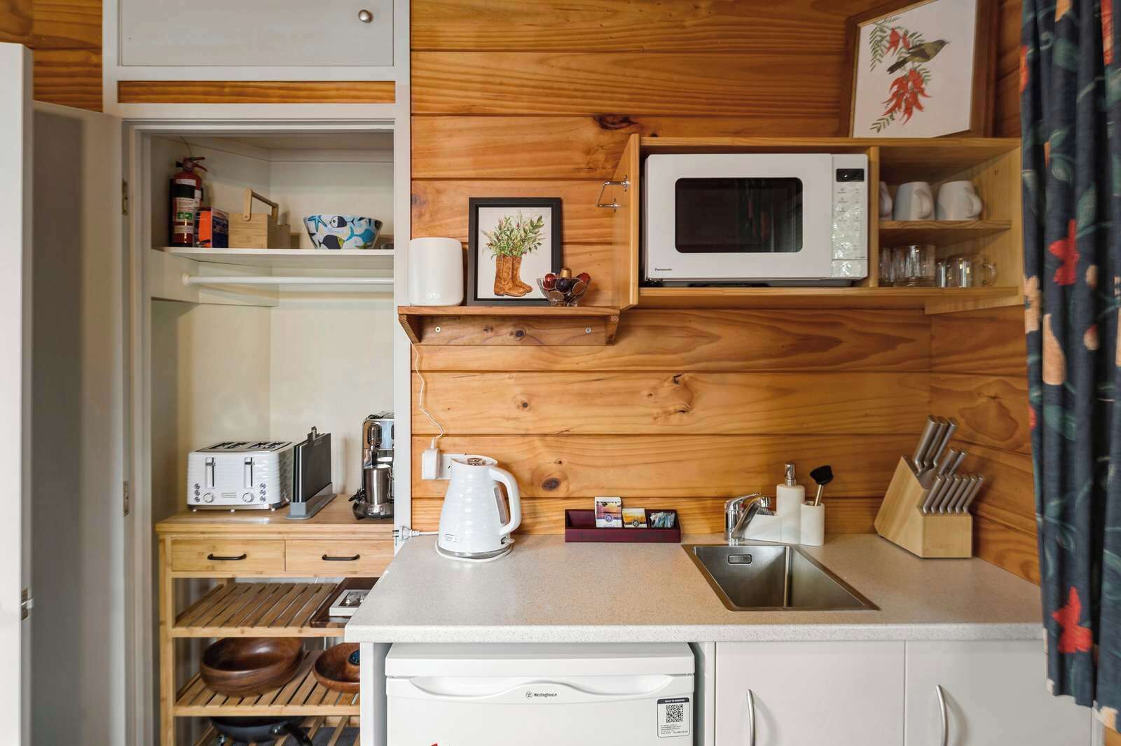A compact kitchen with wooden paneling, a microwave, a kettle, and a sink.