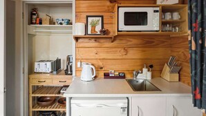Une cuisine compacte avec un revêtement mural en bois, un four à micro-ondes, une bouilloire et un évier.