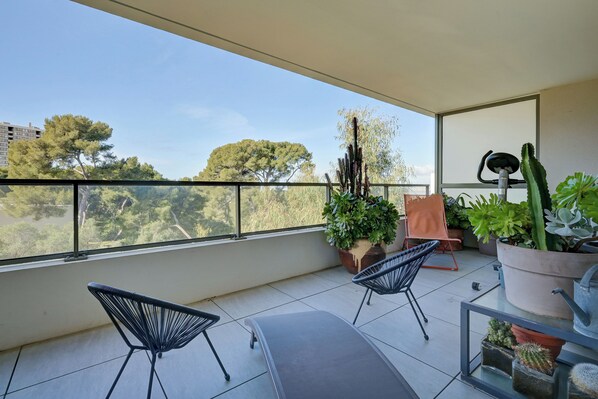 A balcony with two chairs, potted plants, and a view of trees and buildings. - Appartement Floralia - Welkeys (Marseille)