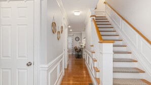 A hallway with a wooden staircase, white walls, and a door. - 15 Min to Boston, Spacious 5BR Retreat on Road with Office Space & Comfortable Beds (Stoneham)