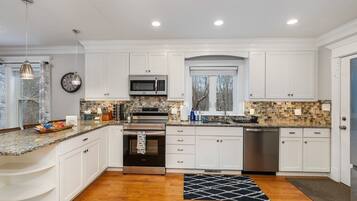 A kitchen with white cabinets, a microwave, an oven, a sink, and a window.