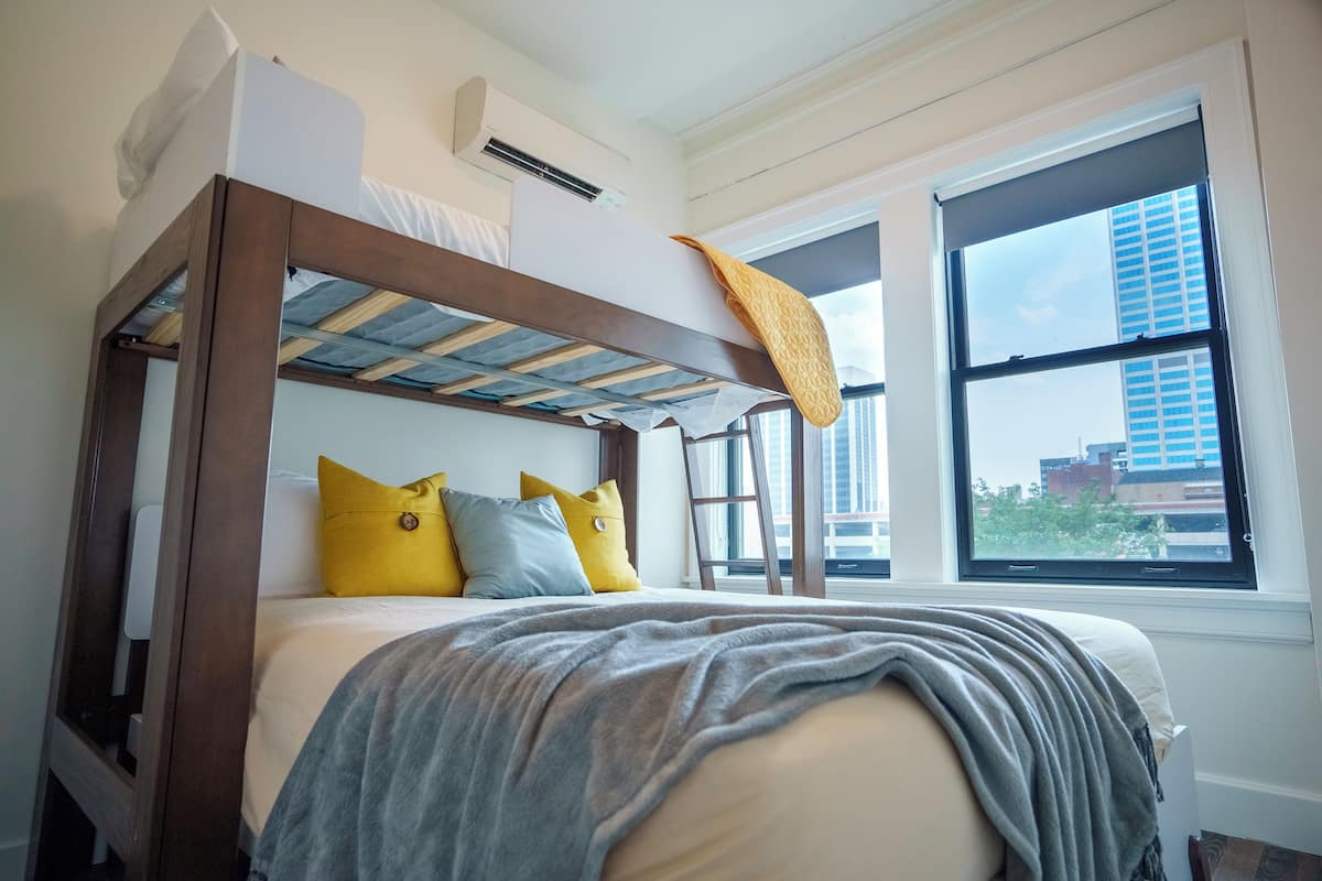 A modern bedroom with a bunk bed, a large window with a city view, and a ceiling fan.
