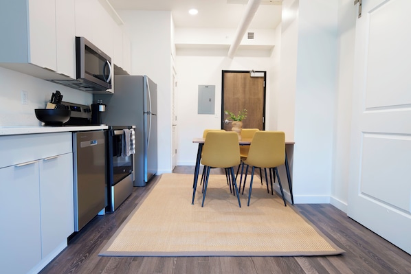 A modern kitchen with white cabinets, a microwave, a refrigerator, and a dining area with a table and chairs. - The Standard in Downtown Columbus (Columbus)