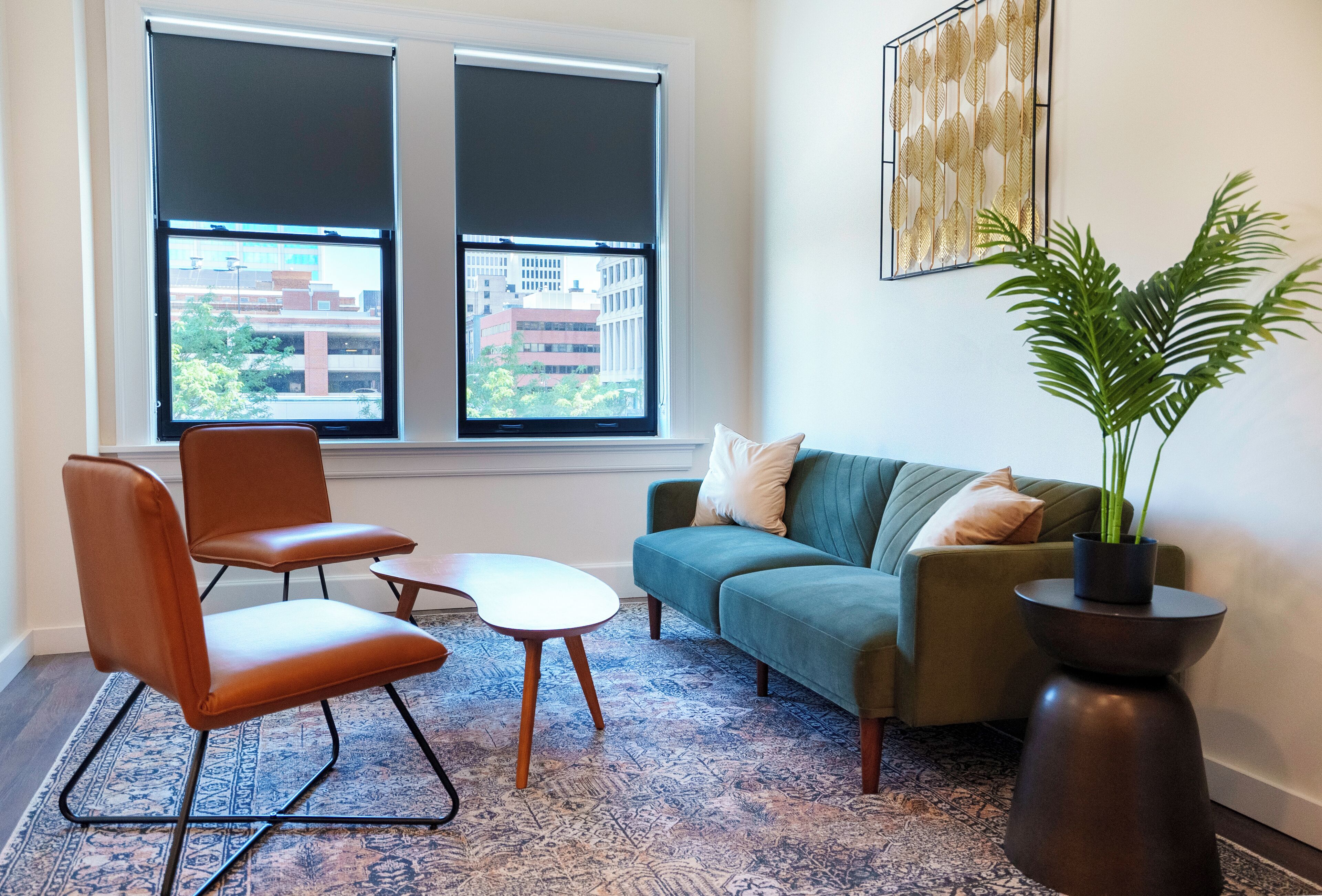 Ein Wohnzimmer mit einer Couch, zwei Sesseln, einem Couchtisch, einer Topfpflanze und einem großen Fenster mit Jalousien.
