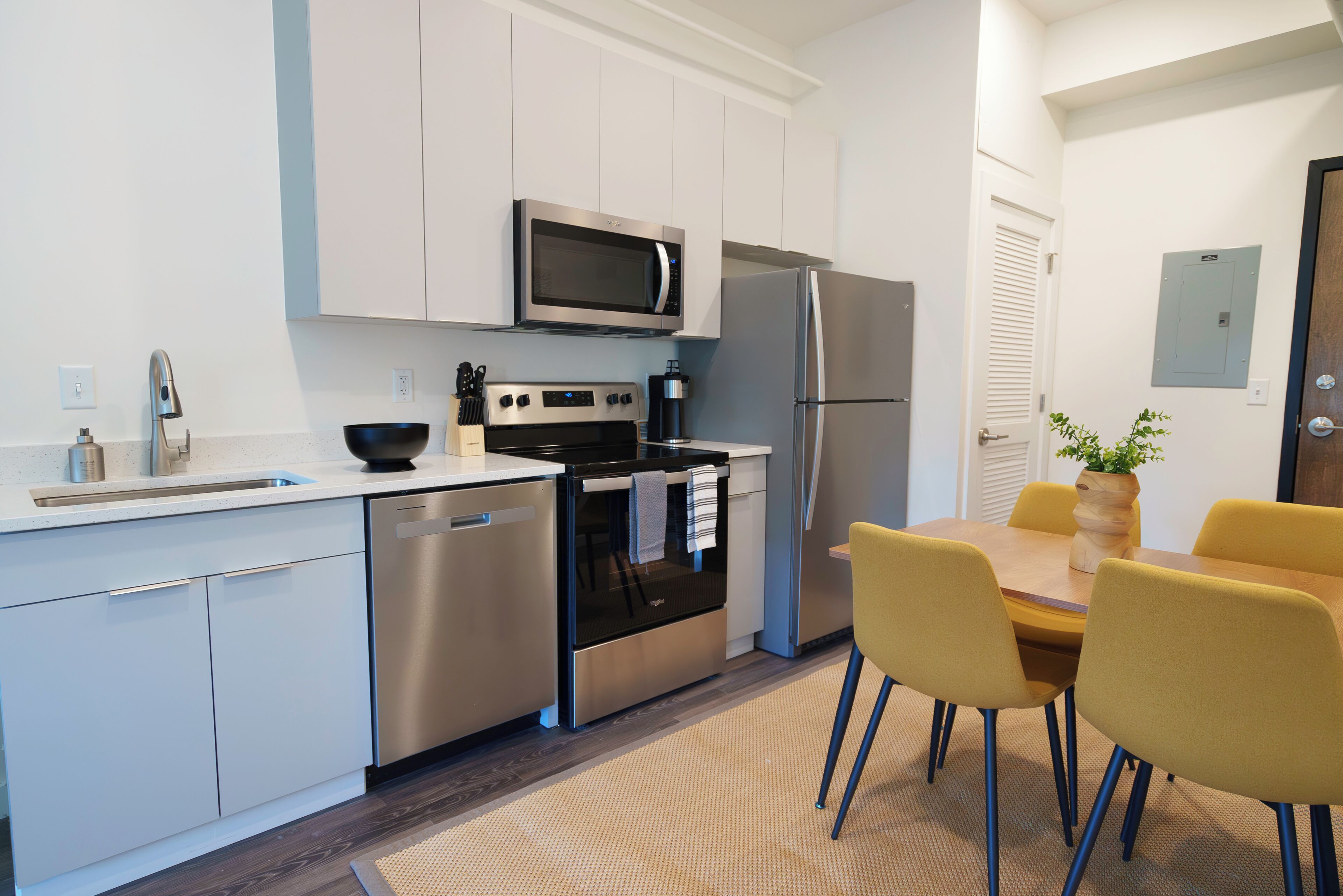 Una cocina moderna con electrodomésticos de acero inoxidable, lavavajillas y un comedor con sillas amarillas.