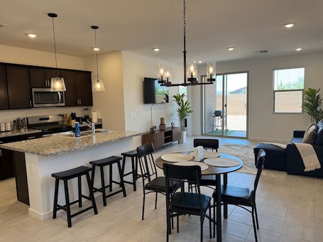 A modern kitchen with a central island, bar stools, and a dining area with a round table and chairs.