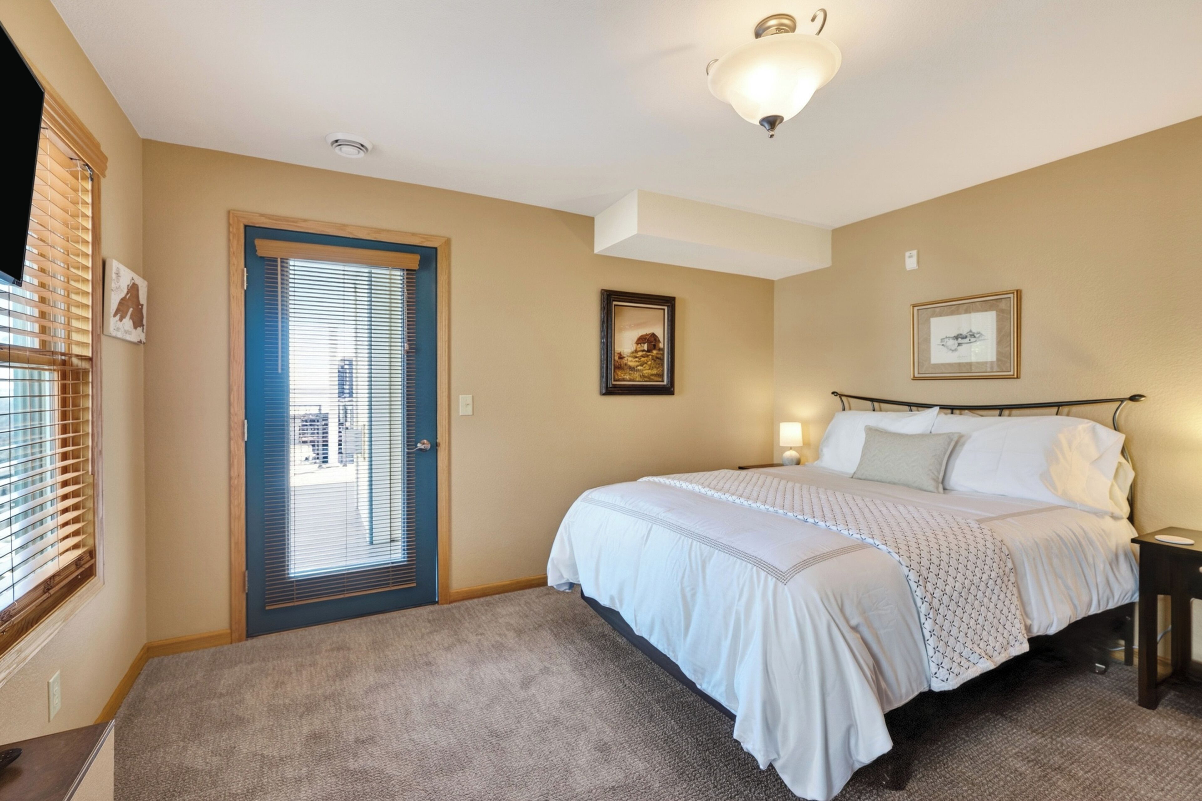 A bedroom with a bed, a door, a window with blinds, and a ceiling light fixture.