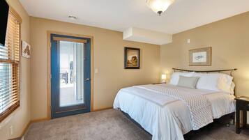 A bedroom with a bed, a door, a window with blinds, and a ceiling light fixture.