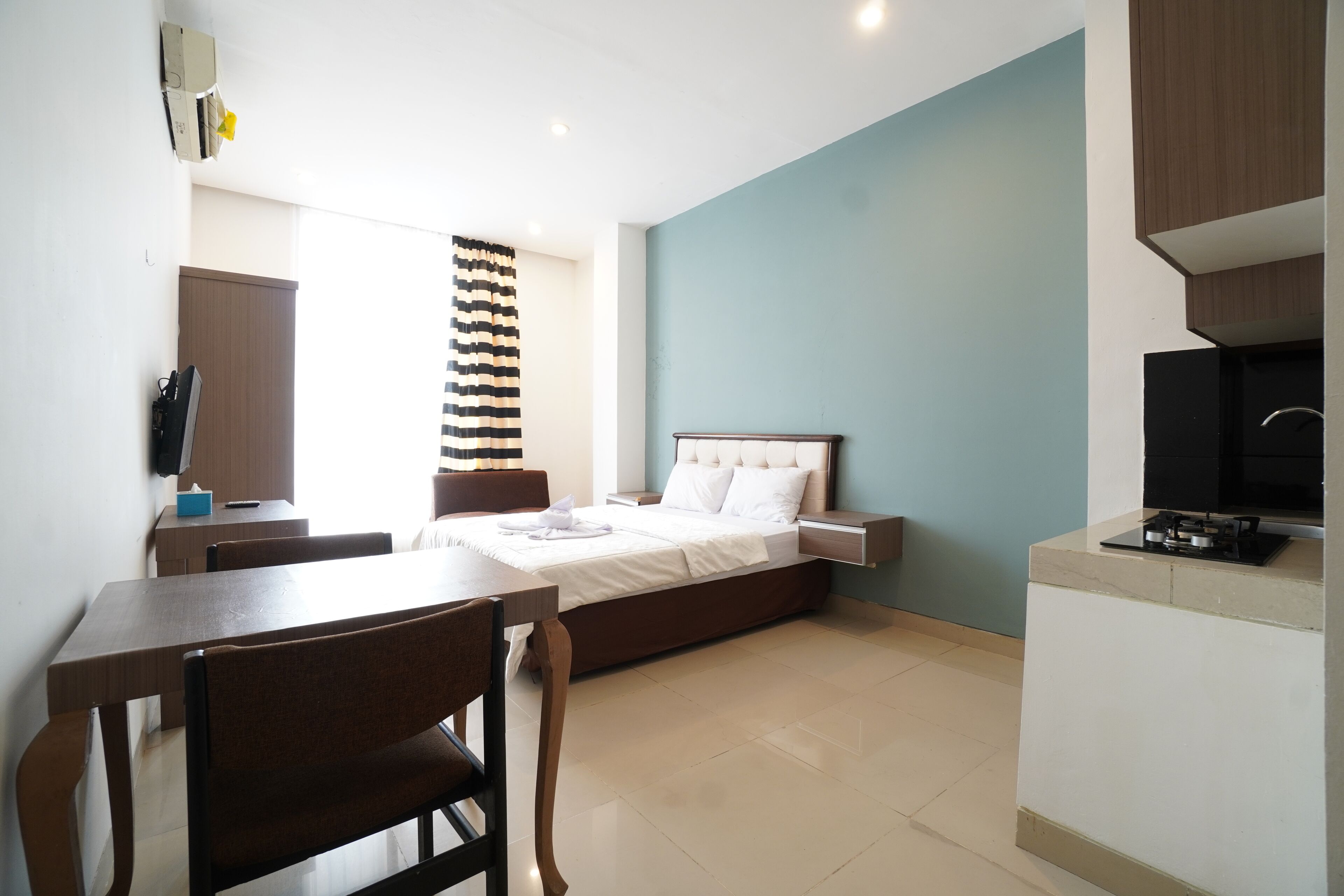 A hotel room with a bed, a desk, a chair, a TV, and a kitchenette.