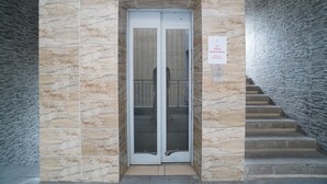 A building entrance with a stone facade and a glass elevator door. - Kamar Bagus (Jakarta)